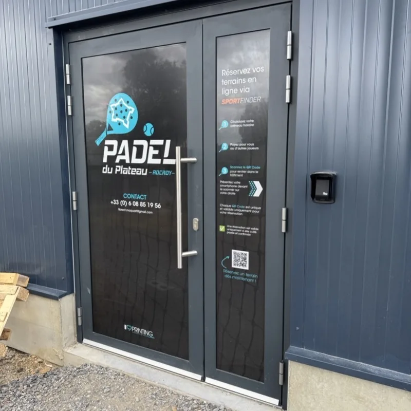 L'entrée vitrée d'un club de padel : sur la porte, le mode d'emploi du QR code d'accès en trois étapes, à côté du lecteur qui l'ouvre