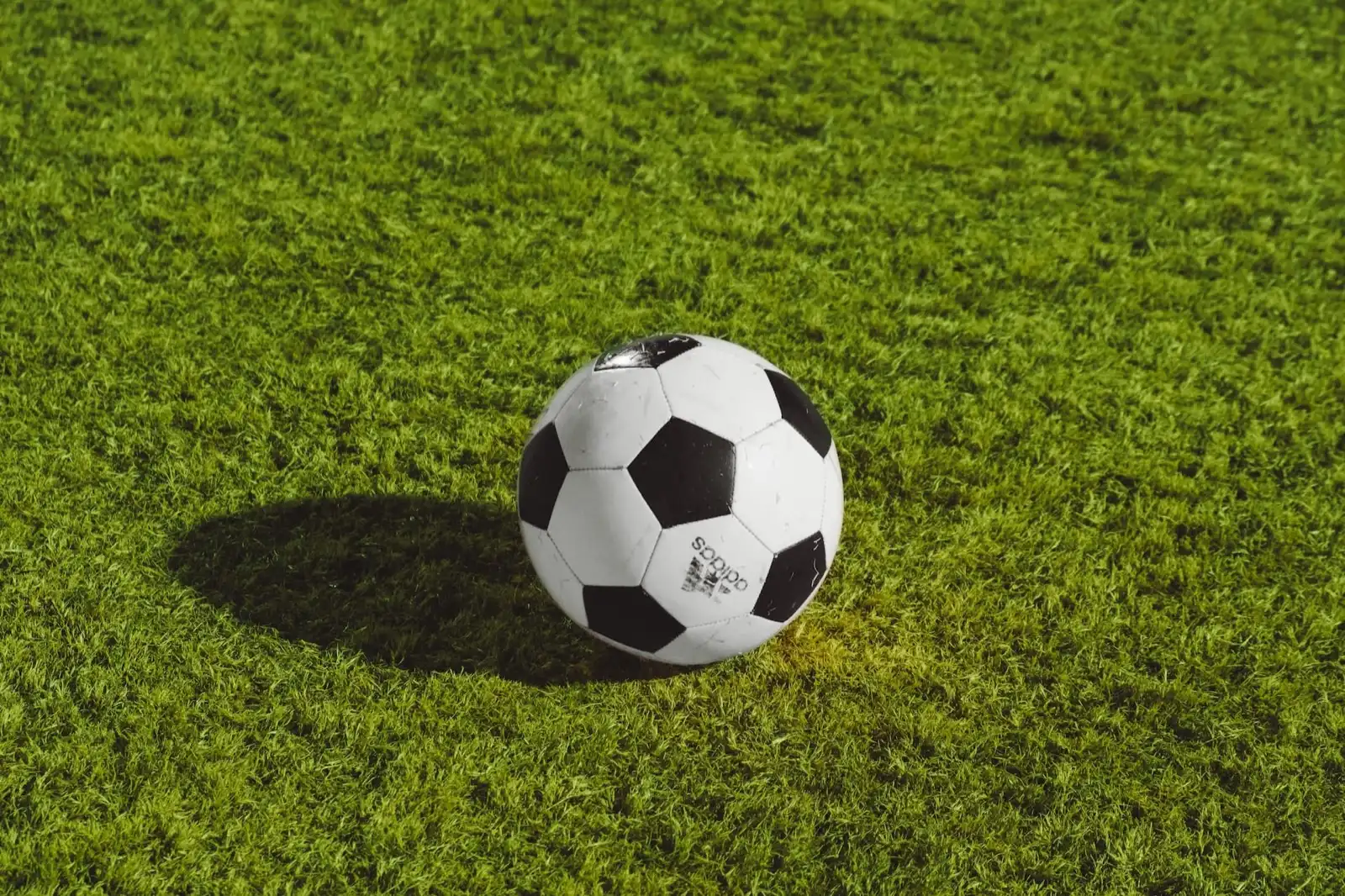 Un ballon de football posé sur le gazon synthétique d'un terrain.