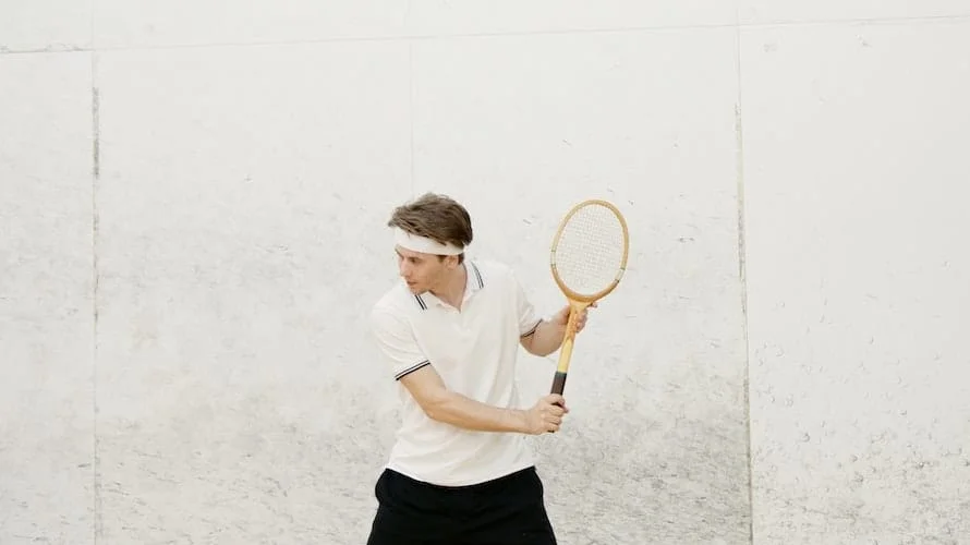 Un joueur de squash en position d'attente, raquette levée, devant le mur blanc du court.
